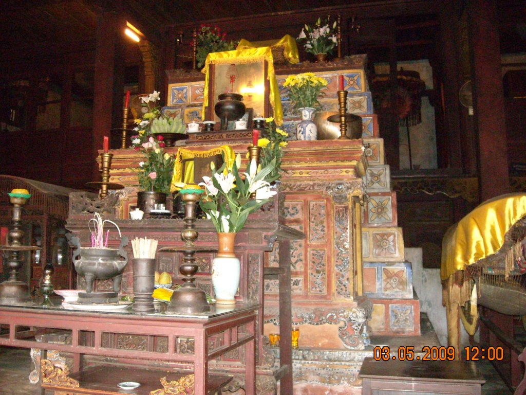 Dimly lit ornate shrine altar with candles, flowers, incense, and decorative tiled steps, warm tones